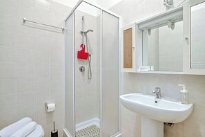 A bathroom with a glass shower enclosure, a white sink, and a toilet with a towel.