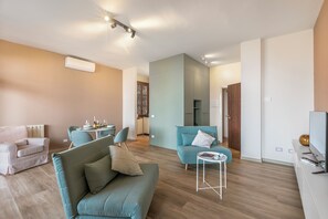 Ein modernes Wohnzimmer mit einer Couch, Sesseln, einem kleinen Tisch und einem Fernseher.