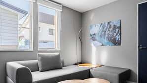 Ett modernt rum med en grå soffa, ett runt träbord och ett stort fönster med utsikt över ett snötäckt landskap.