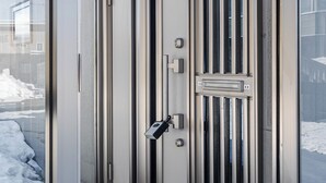 Une porte blindée dotée d’un clavier et d’un judas, une porte vitrée, et une vue sur une rue enneigée.
