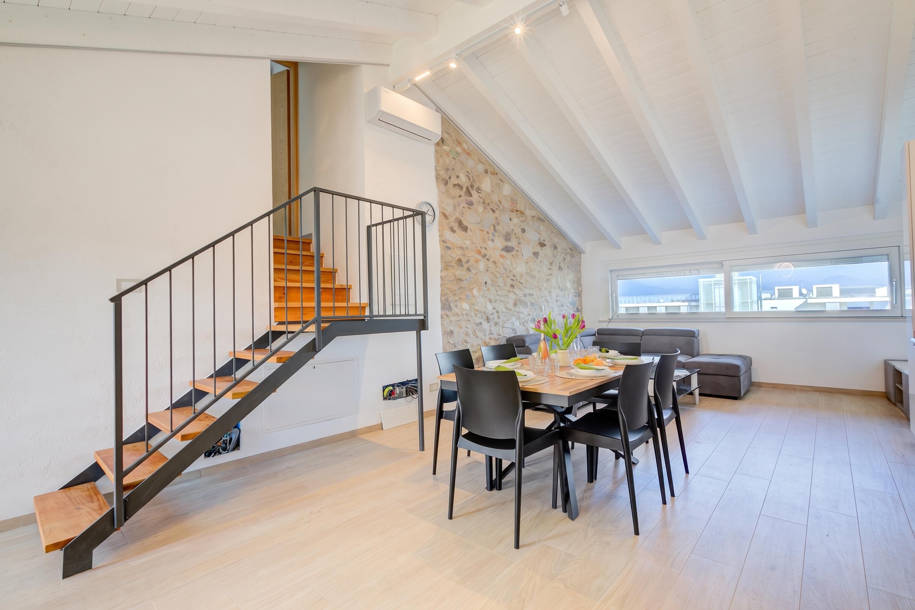 Ein modernes Interieur mit einer Holztreppe, einem Essbereich mit Tisch und Stühlen sowie einer Steinwand.