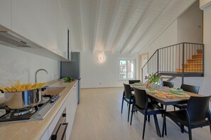 A modern kitchen with a stove, pots, and a dining area with chairs and a table. - Peschiera 2BR Lake View + Parking, Peschiera del Garda, Italy (Peschiera del Garda)