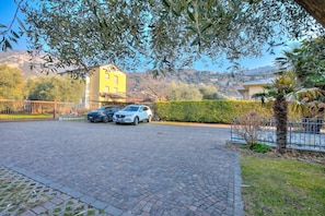 A paved parking area with two cars, a yellow building in the background, and a clear sky. - Agritur Laura- Sogno zen 6 with Shared Garden, Torbole sul Garda, Italy (Torbole sul Garda)