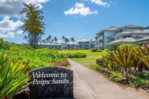 Ein Weg, der zu einem Resort führt, mit einem Schild, auf dem 'Willkommen bei Poipu Sands' steht.