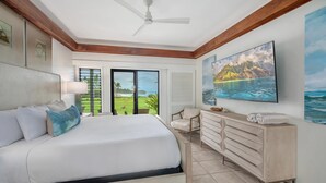 A bedroom with a bed, a dresser, a chair, a ceiling fan, and a large window with a view of the outdoors. - Poipu Sands Unit 514 Oceanfront 2 Bedroom 2 Bath (Poipu)