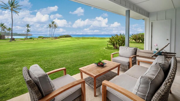 A covered outdoor seating area with a view of a golf course and ocean. - Poipu Sands Unit 514 Oceanfront 2 Bedroom 2 Bath (Poipu)