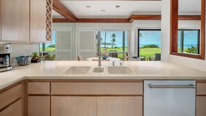 A modern kitchen with a large island, built-in appliances, and a view of the ocean. - Poipu Sands Unit 514 Oceanfront 2 Bedroom 2 Bath (Poipu)