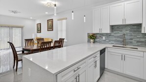 Una cocina moderna con armarios blancos, encimera de granito, iluminación colgante y salpicadero de azulejos.