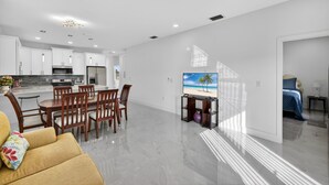 Un espacio de estar moderno con comedor, cocina y un televisor mostrando una escena de playa.