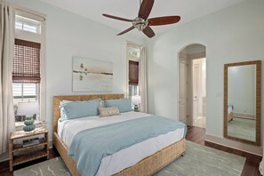A bedroom with a bed, a ceiling fan, a window with blinds, a bedside table with a lamp, and a painting on the wall. - Sage & Sand: Golf Cart, Bikes & Pickleball (Santa Rosa Beach)