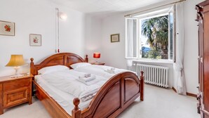 Ein Schlafzimmer mit einem hölzernen Bett, Nachttischen, einem Fenster mit Blick auf Palmen und einer Heizung.