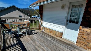 Une terrasse en bois avec une porte de garage blanche, un mur de pierre et un ciel d’un bleu limpide.