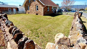 Une maison en pierre avec un toit en pente, un mur de pierre et une cour couverte d’herbe.