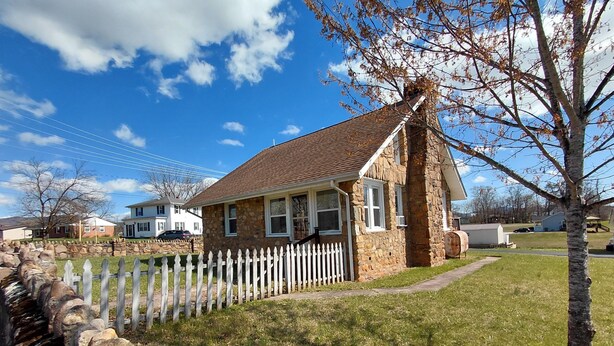 Une maison en pierre avec une clôture blanche en bois, une cour verdoyante et un ciel bleu dégagé.