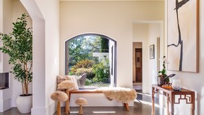 Un interno moderno con un'ampia finestra ad arco, una panca e un tavolino con oggetti decorativi.