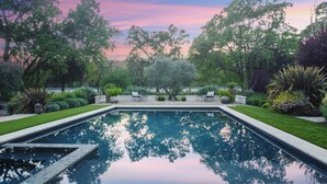 Una piscina rettangolare con un bordo circostante, circondata da erba ben curata e diverse piante.