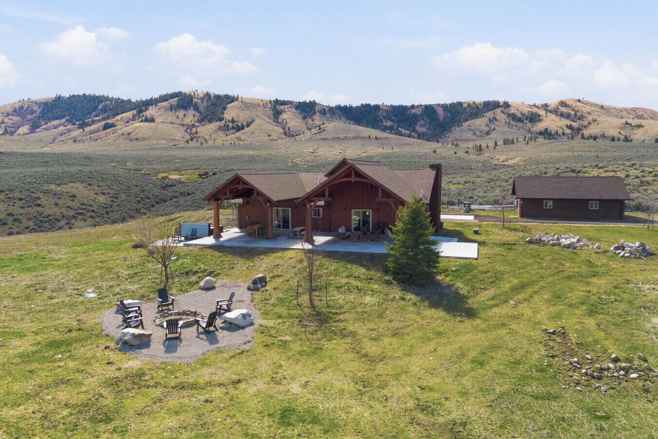 A wooden cabin with a porch, outdoor seating, and a view of rolling hills.