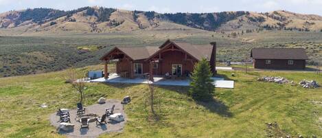 A wooden cabin with a porch, outdoor seating, and a view of rolling hills.