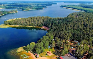 Ilmakuva metsäisestä alueesta, jossa on järvi, useita pieniä saaria sekä muutamia rakennuksia, kuten mökki ja pieni rakennelma.