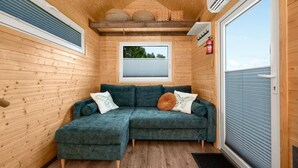 A cozy corner with a green sectional sofa, a small window, and a fire extinguisher on the wall. - Lovely home in Niedzwiedz with sauna (Niedzwiedz)
