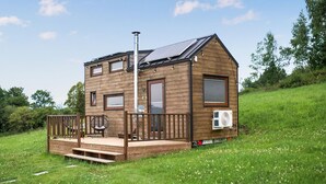 A small wooden cabin with a deck, solar panels, and an air conditioning unit. - Lovely home in Niedzwiedz with sauna (Niedzwiedz)