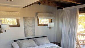 Quarto com estrutura de cama de madeira, mesa de cabeceira, tapete estampado e janela com vista para árvores.