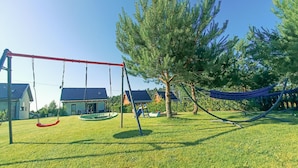 A playground with swings and a hammock, surrounded by grass and trees. - 3 bedroom stunning home in Odargowo (Odargowo)