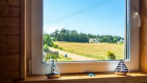 A window with a view of a rural landscape, a small boat, and a sailboat model on the windowsill. - 3 bedroom stunning home in Odargowo (Odargowo)