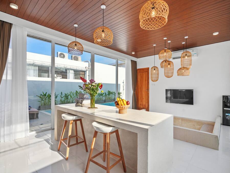 Una cocina moderna con una isla central, taburetes de bar, luces colgantes y vistas al exterior.