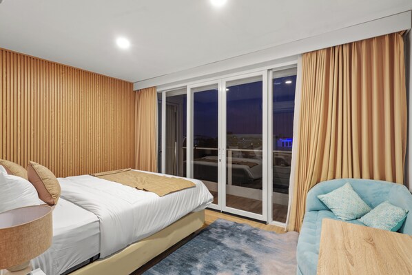 A hotel room with a bed, a sofa, a table, and a sliding glass door leading to a balcony. - Lux Villages and K Hotel (Keroboken Kelod)