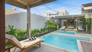 Un'area piscina con lettini, una spa con vetrate e vegetazione circostante.