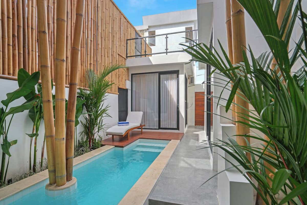 A modern outdoor pool area with a lounge chair, bamboo privacy screen, and a view of the building.
