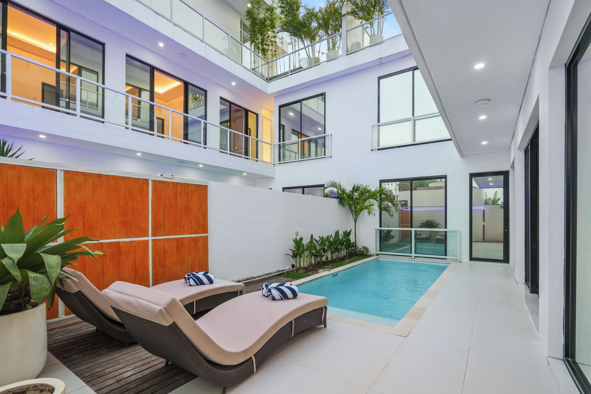 Un moderno edificio residencial de varios niveles con piscina, sillas de descanso y plantas en macetas.