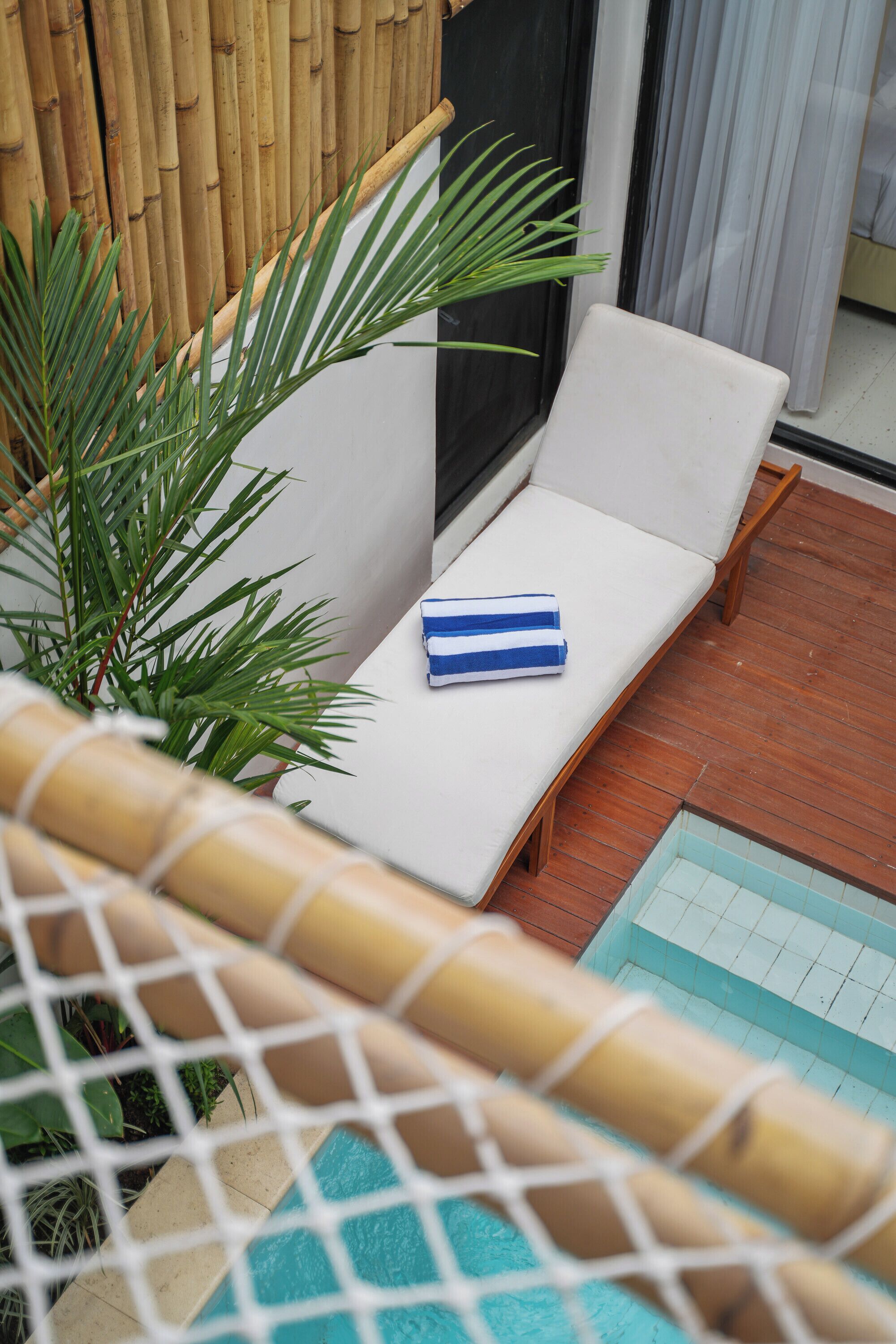 A sun lounger with a towel, a small pool, and a bamboo fence.
