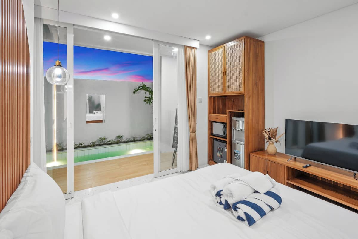 A modern hotel room with a bed, a TV, a wooden cabinet, and a sliding glass door leading to a balcony.