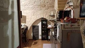 A rustic kitchen with stone walls, a tiled floor, a refrigerator, and a dining area with chairs and a table. - Studio directly in the historic center (Giovinazzo)