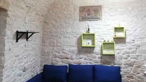 A room with a stone wall, a blue sofa, and green shelves. - Studio directly in the historic center (Giovinazzo)