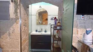 A bathroom with a stone wall, a mirror, a sink, and a shower area. - Studio directly in the historic center (Giovinazzo)