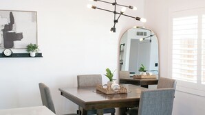 A dining area with a wooden table, grey upholstered chairs, a black chandelier, a round mirror, and a wall-mounted clock. - Charming 3-bedroom house in peaceful Tempe minutes from the Aiport (Tempe)