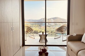 Ein modernes Wohnzimmer mit einem großen Fenster, zwei Korbstühlen, einem runden Tisch und einer Couch.