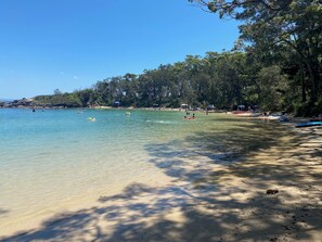 Uma praia com água cristalina, árvores e pessoas.