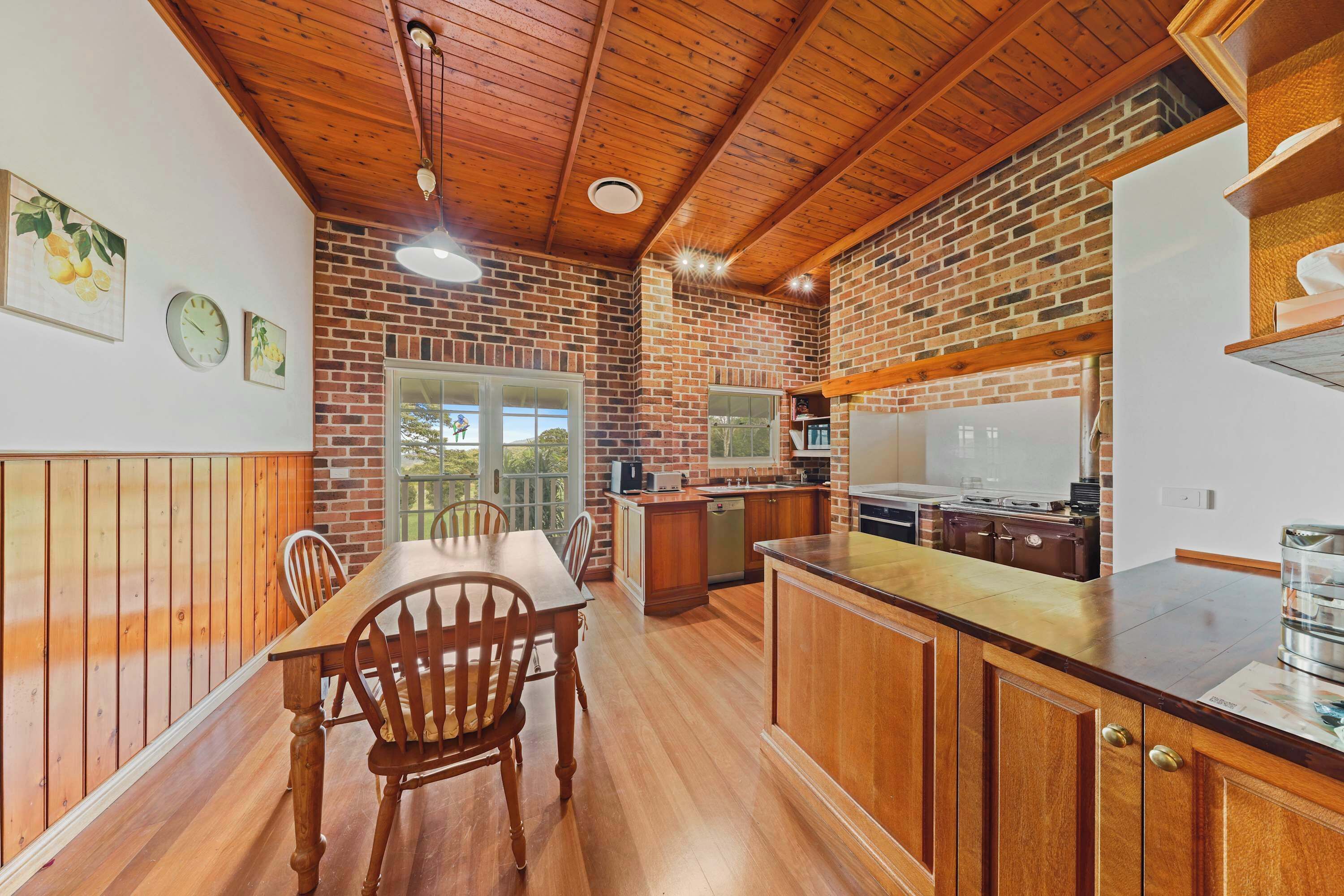 A kitchen with wooden cabinets, a dining table, and a brick wall.