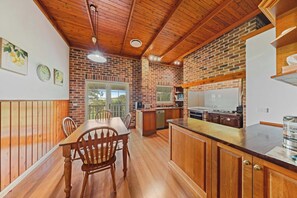 A kitchen with wooden cabinets, a dining table, and a brick wall. - Valley View Retreat  Private 36 Acre Hinterland Escape (Witta)