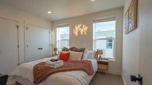 A bedroom with a bed, bedside tables, a wall-mounted neon sign, and a window. - Modern Townhome 10 min to Downtown + Airport (Salt Lake City)
