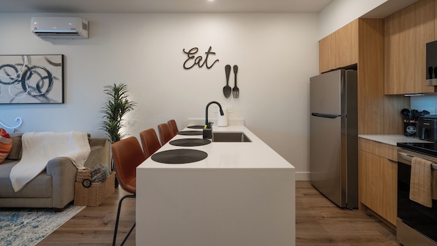 A modern kitchen with a central island, a dining area with chairs, a sofa, and a wall-mounted 'Eat' sign. - Modern Townhome 10 min to Downtown + Airport (Salt Lake City)