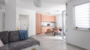 Een modern appartement met een grijze bank, een eethoek met roze stoelen en een keuken met perzikkleurige kastjes.
