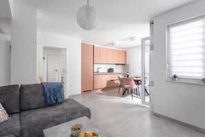 Eine moderne Wohnung mit einem grauen Sofa, einem Essbereich mit rosafarbenen Stühlen und einer Küche mit Pfirsichfarbenen Schränken.
