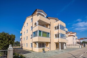 Un immeuble résidentiel à plusieurs étages, doté de balcons, d’une allée pavée et surplombant un ciel dégagé.