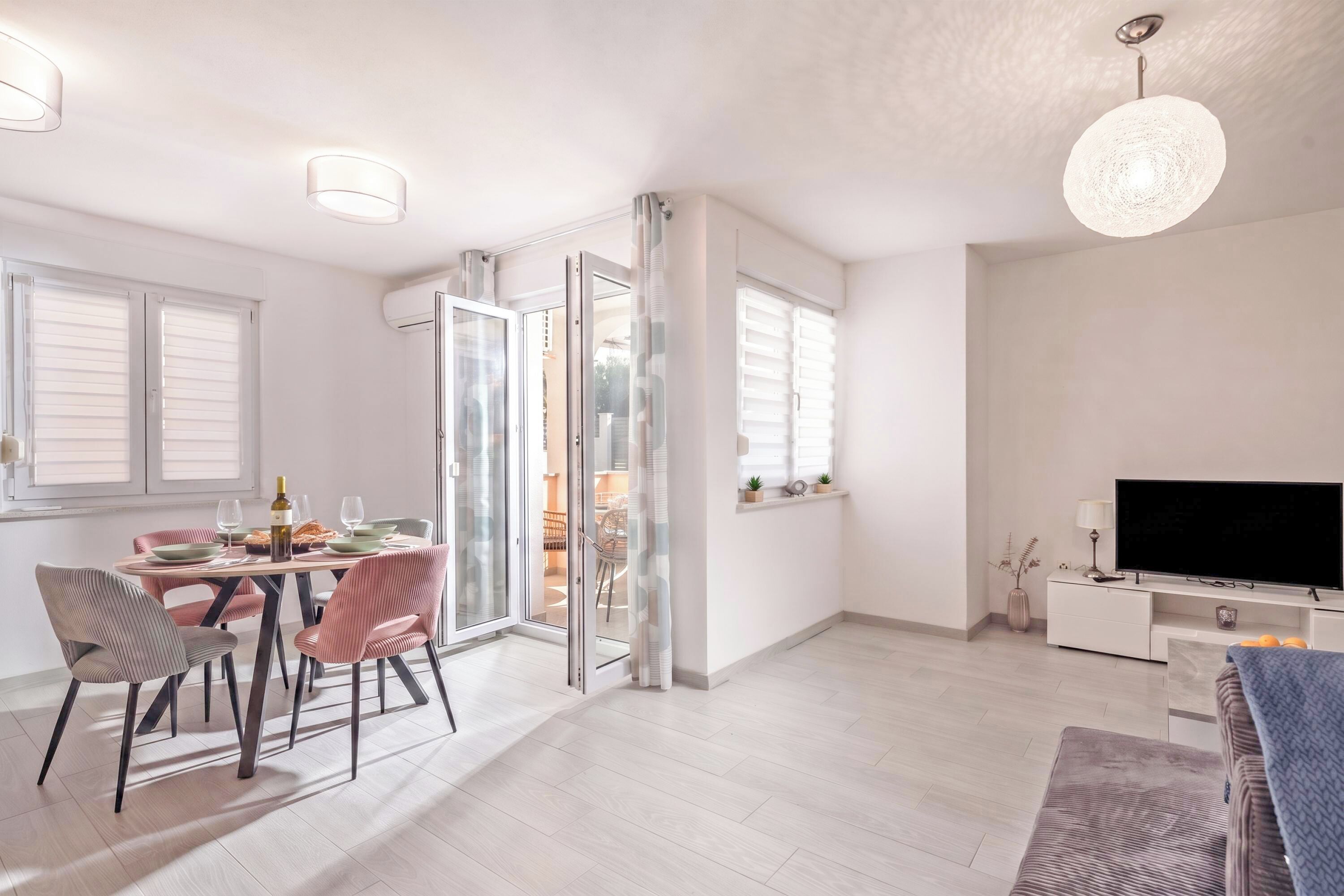 A modern living room with a dining area, a flat-screen TV, and a sliding glass door leading to an outdoor space.