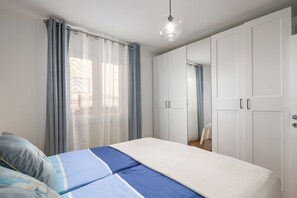 Ein Schlafzimmer mit Bett, Vorhängen, einem Kleiderschrank und einer Pendelleuchte.